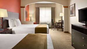 A hotel room with two beds, a desk, a television, and a chair.