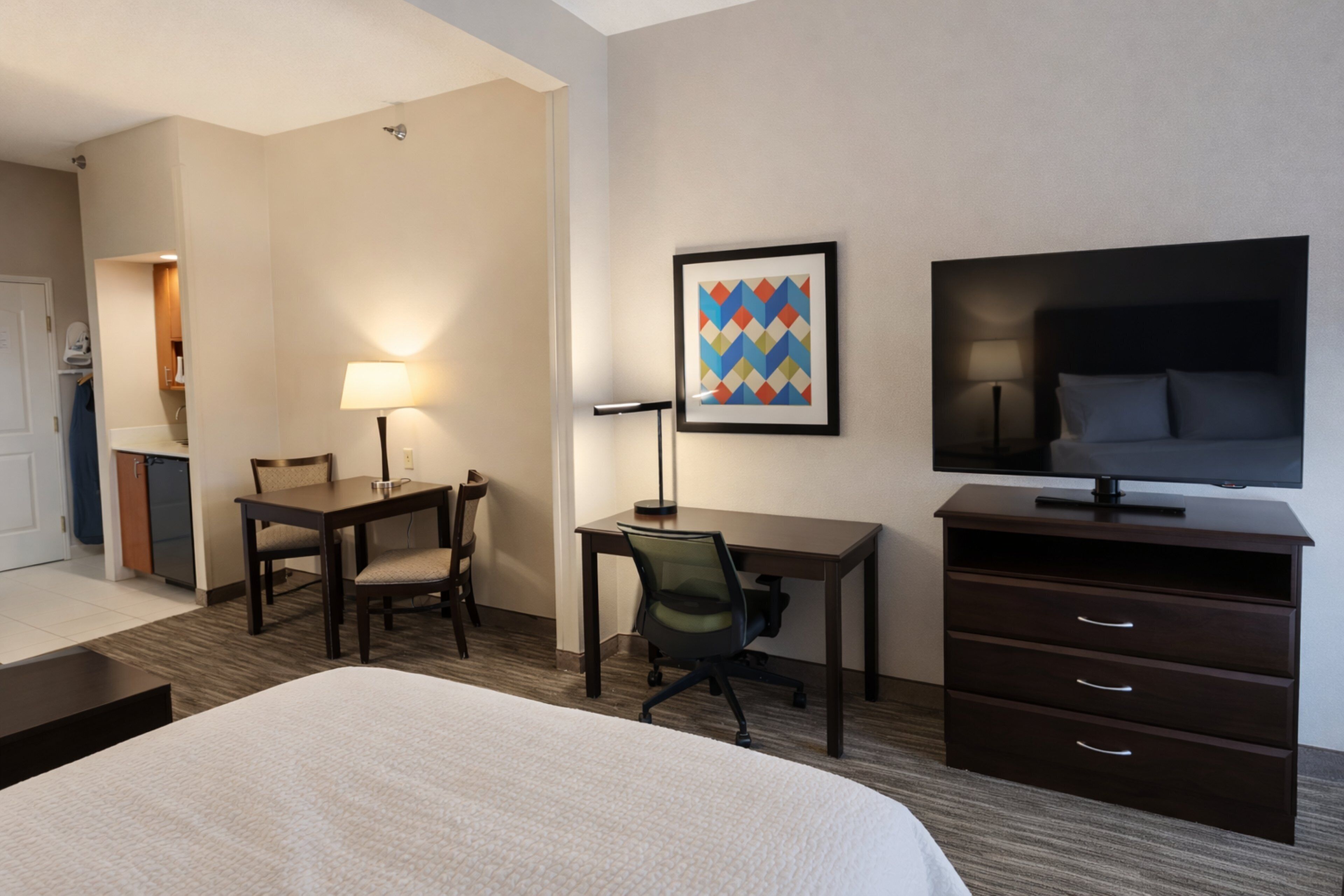 A hotel room with a bed, desk, chair, TV, and a framed picture on the wall.
