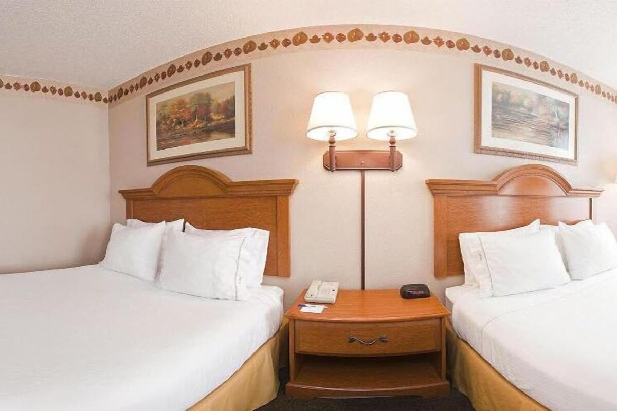 Una habitación de hotel con dos camas, una mesita de noche con un teléfono y una lámpara, y dos lámparas de pared.
