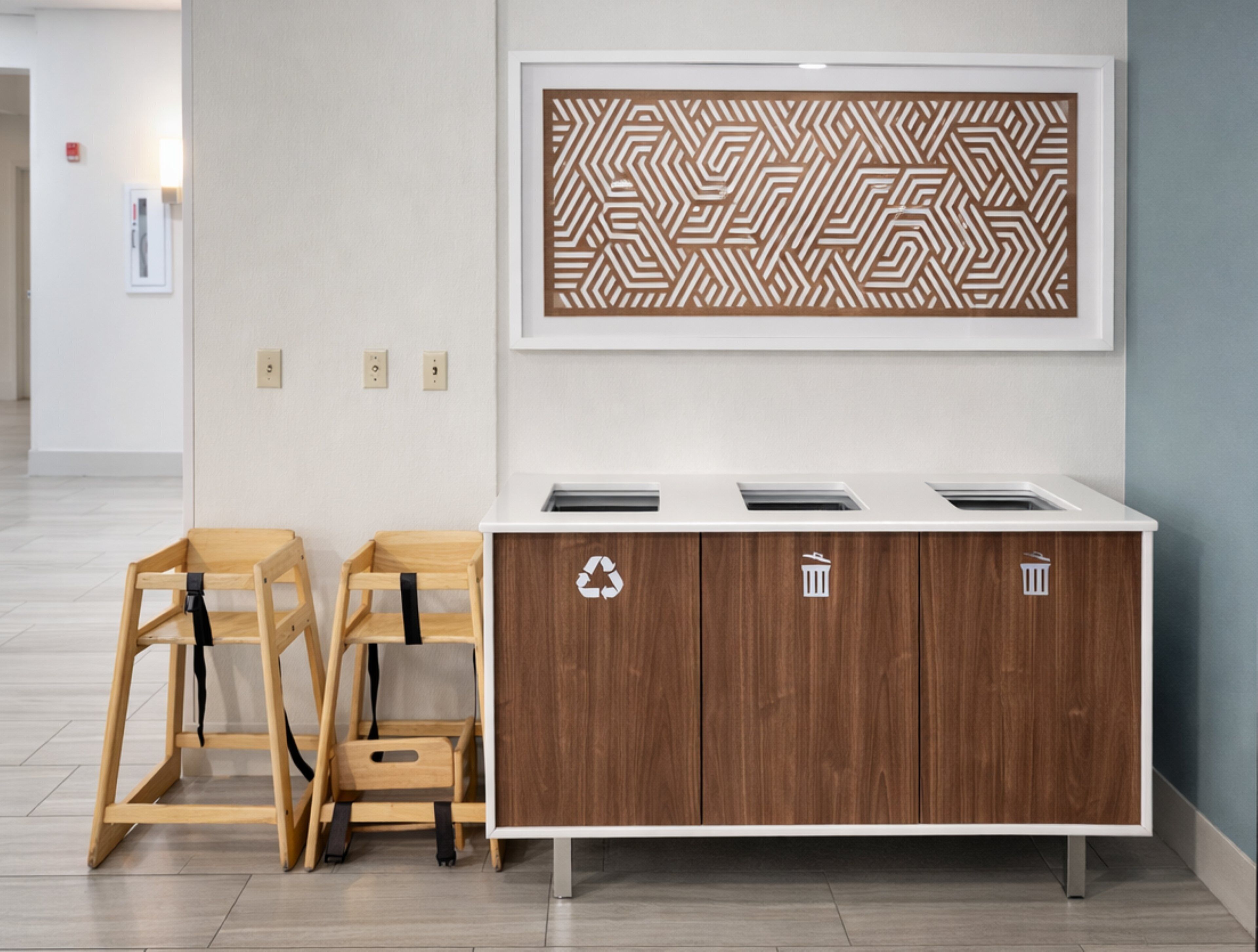 A modern restroom with a wooden cabinet, a recycling bin, and a framed geometric artwork on the wall.