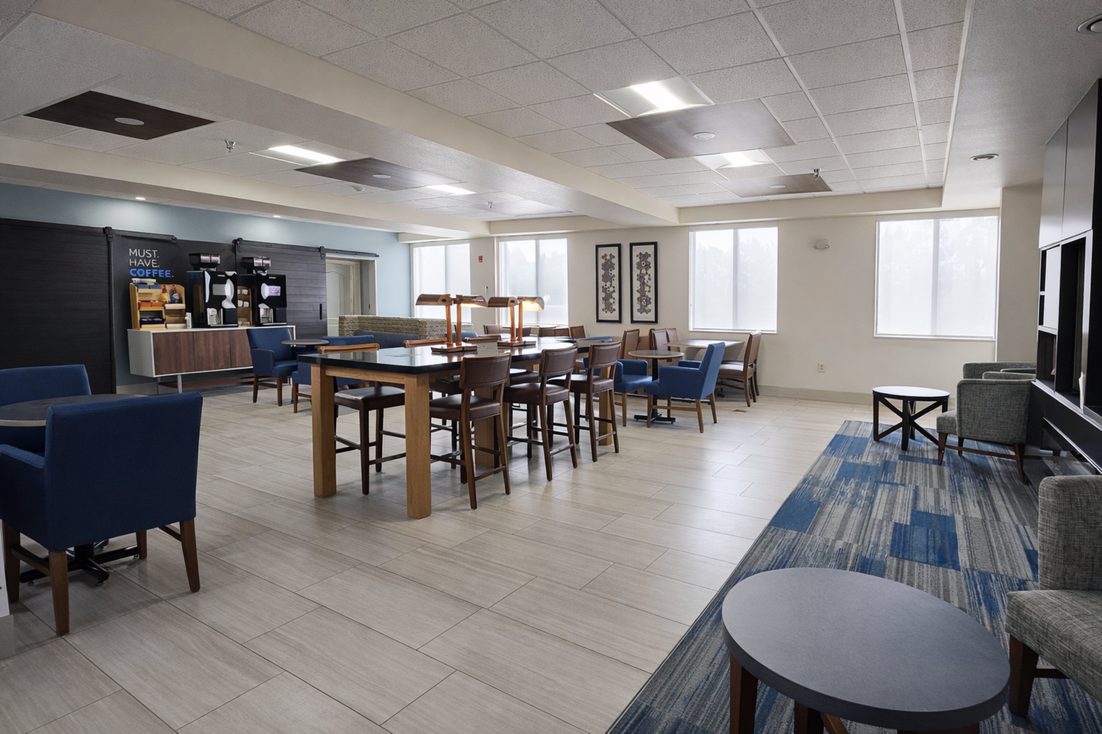 A spacious indoor area with multiple seating arrangements, a coffee station, and large windows providing natural light.
