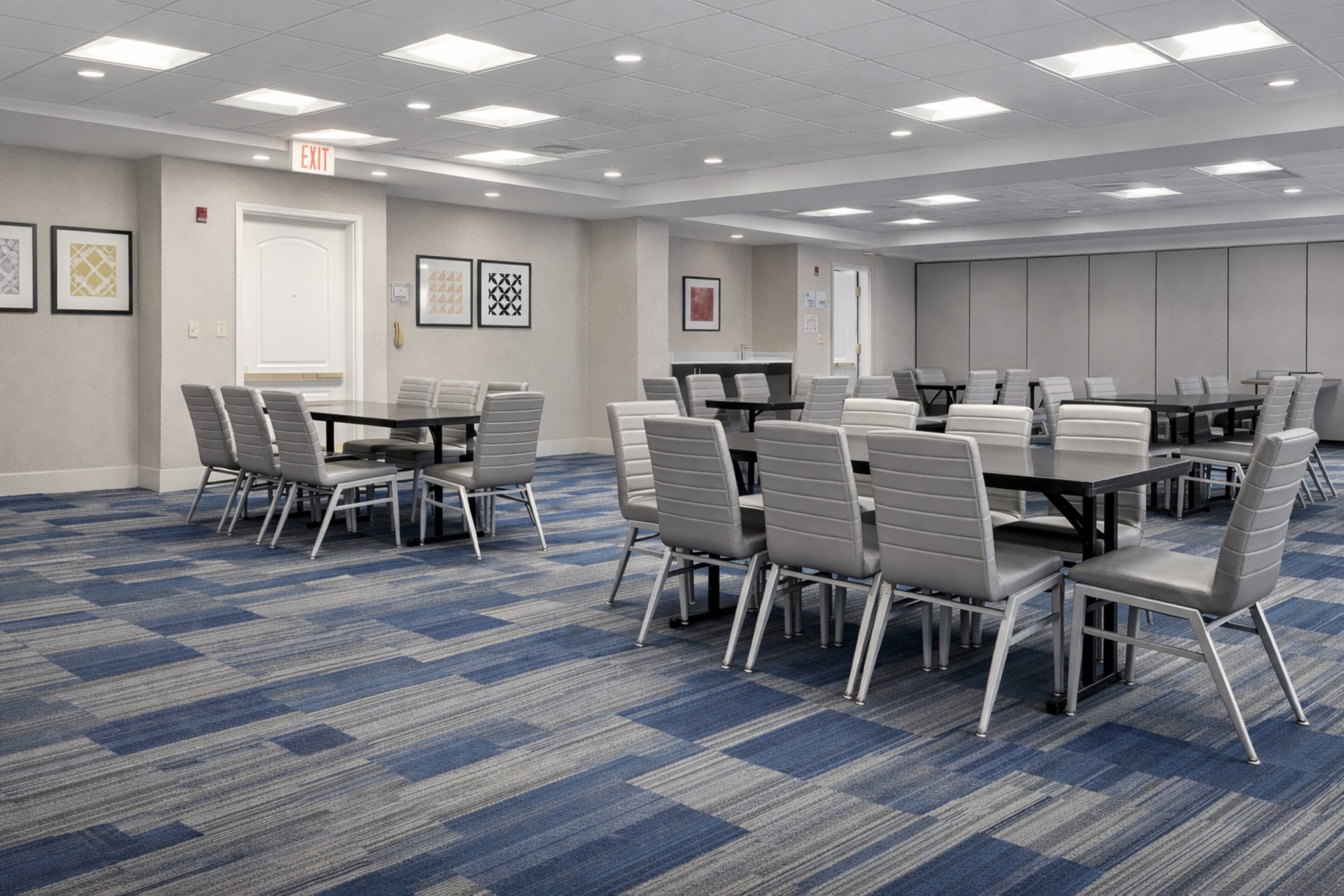 A conference room with a blue carpet, gray chairs, and tables.