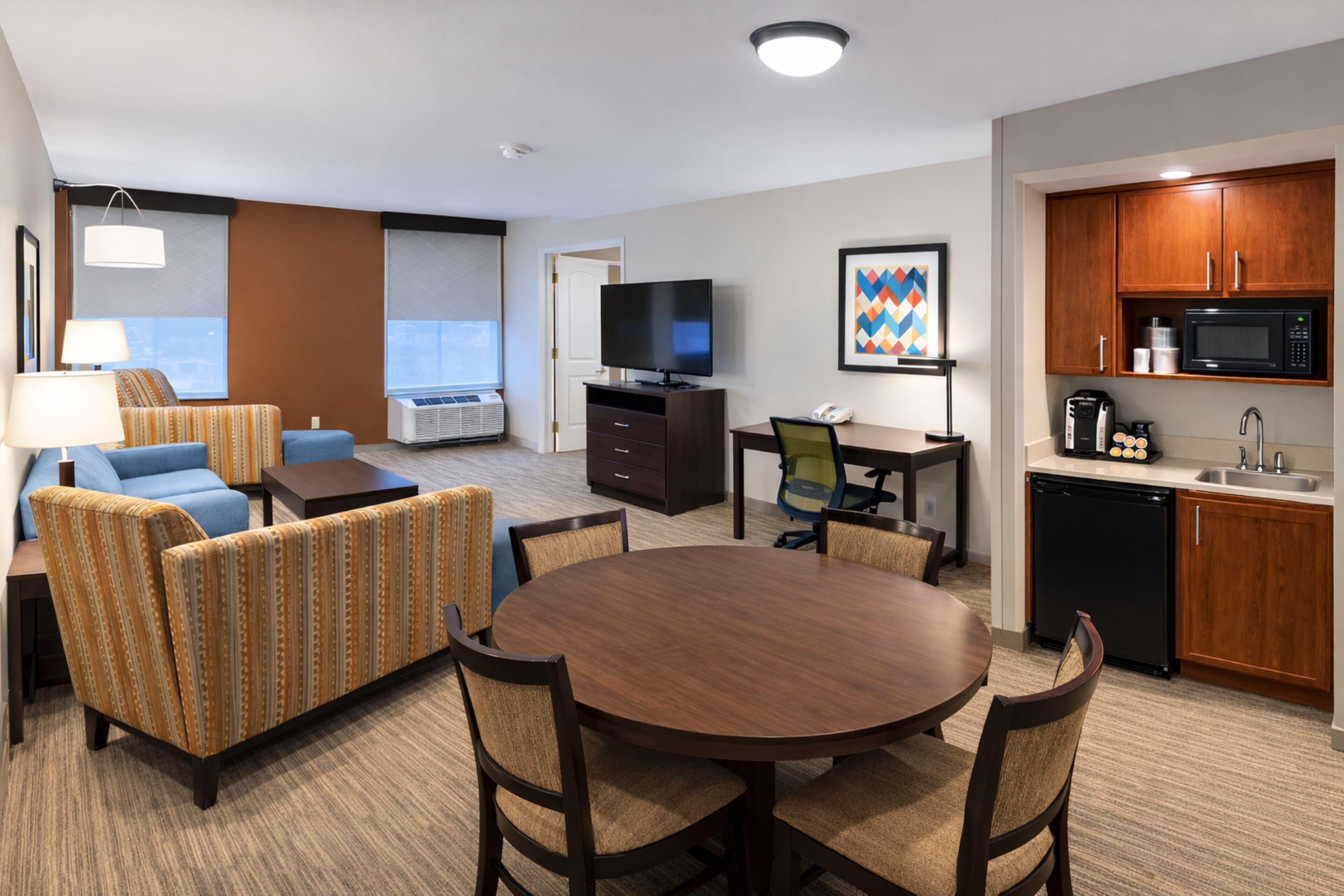 Een hotelkamer met een eethoek, een televisie, een kitchenette en een groot raam.