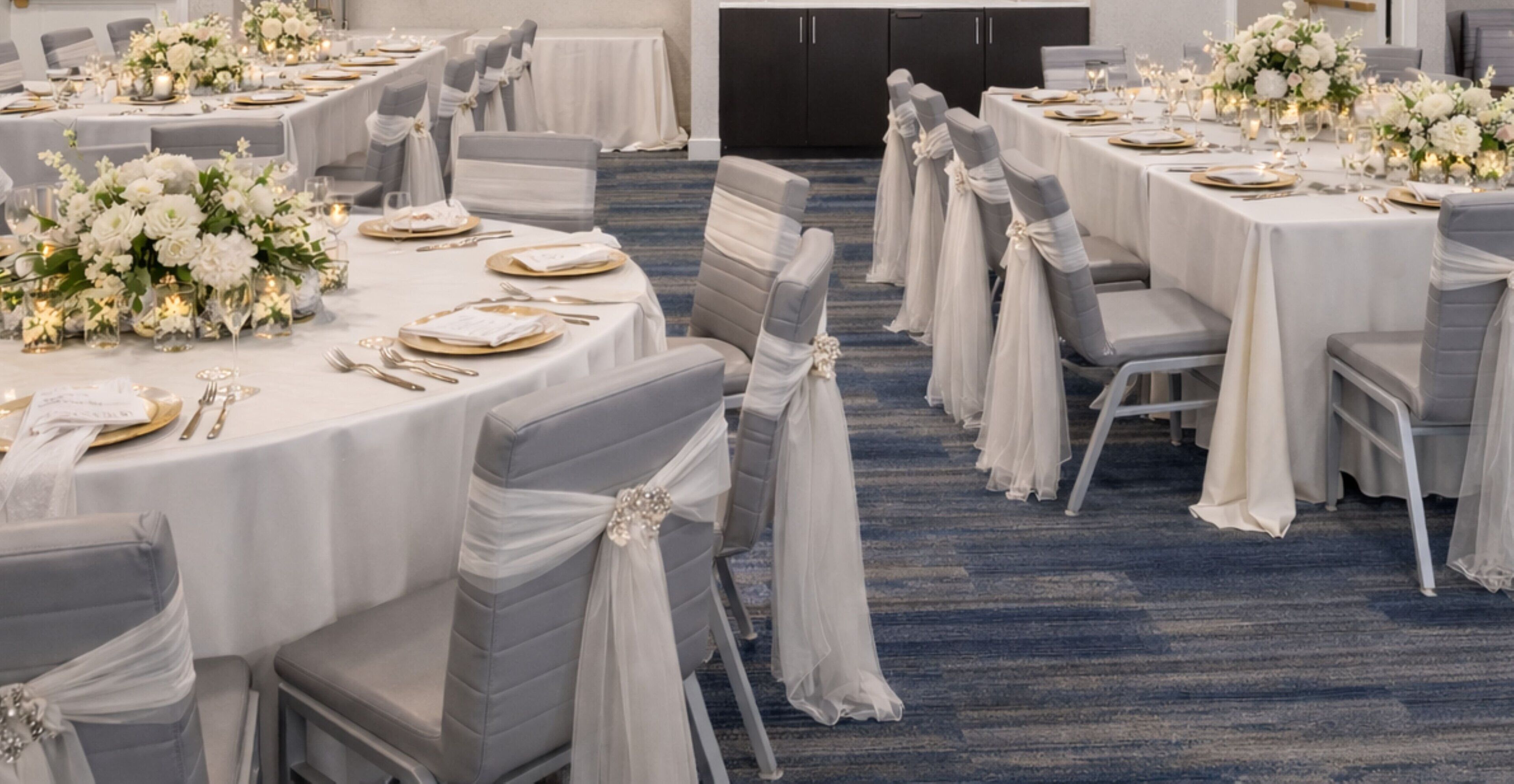 A banquet hall with round tables, grey chairs, and white tablecloths.