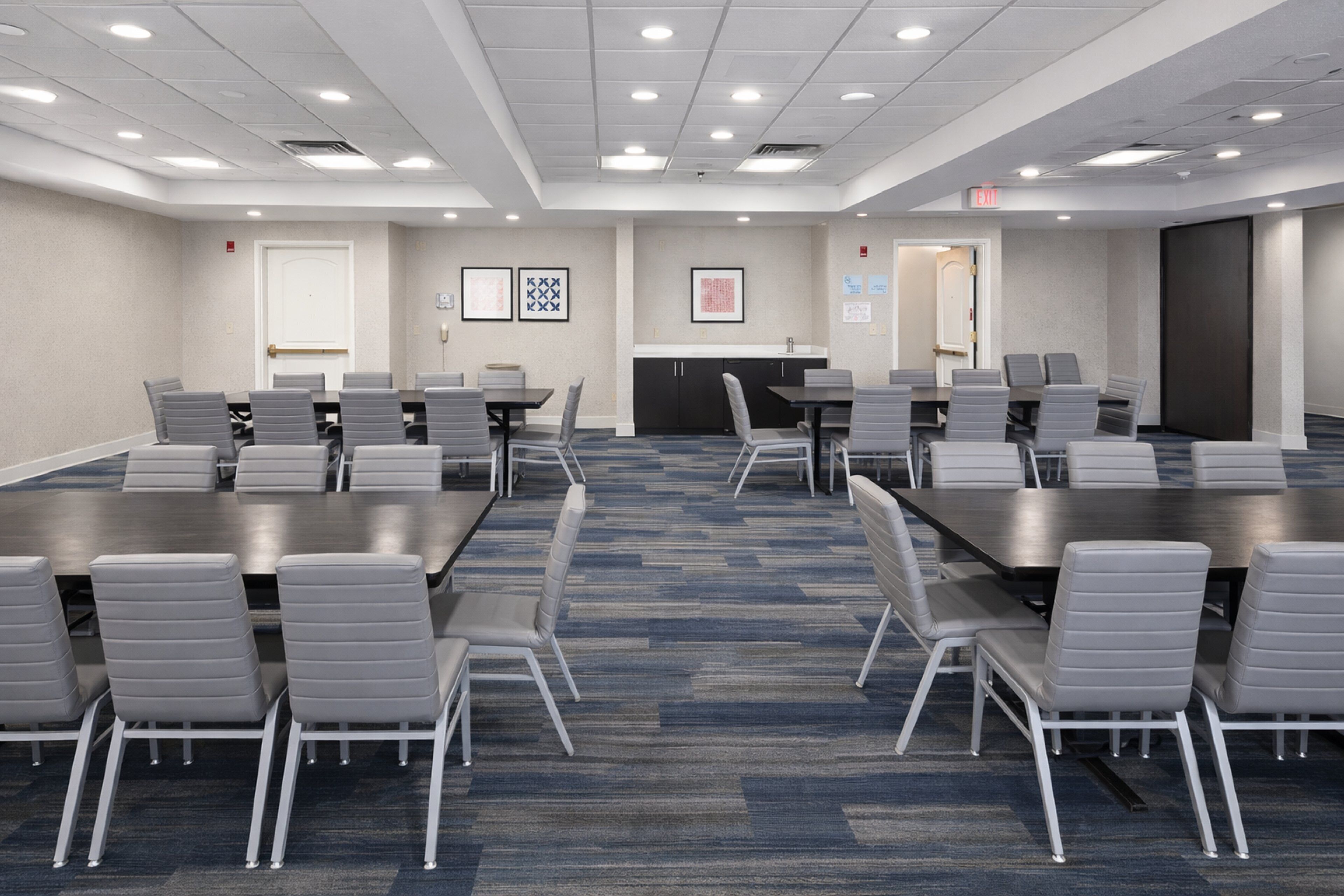A conference room with tables and chairs, a kitchenette, and framed pictures on the walls.