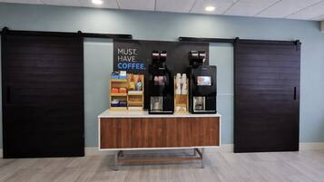 Een koffiehoek met twee espresso machines, een bord waarop staat 'COFFEE IS ESSENTIEEL' en een plank met diverse koffieproducten.
