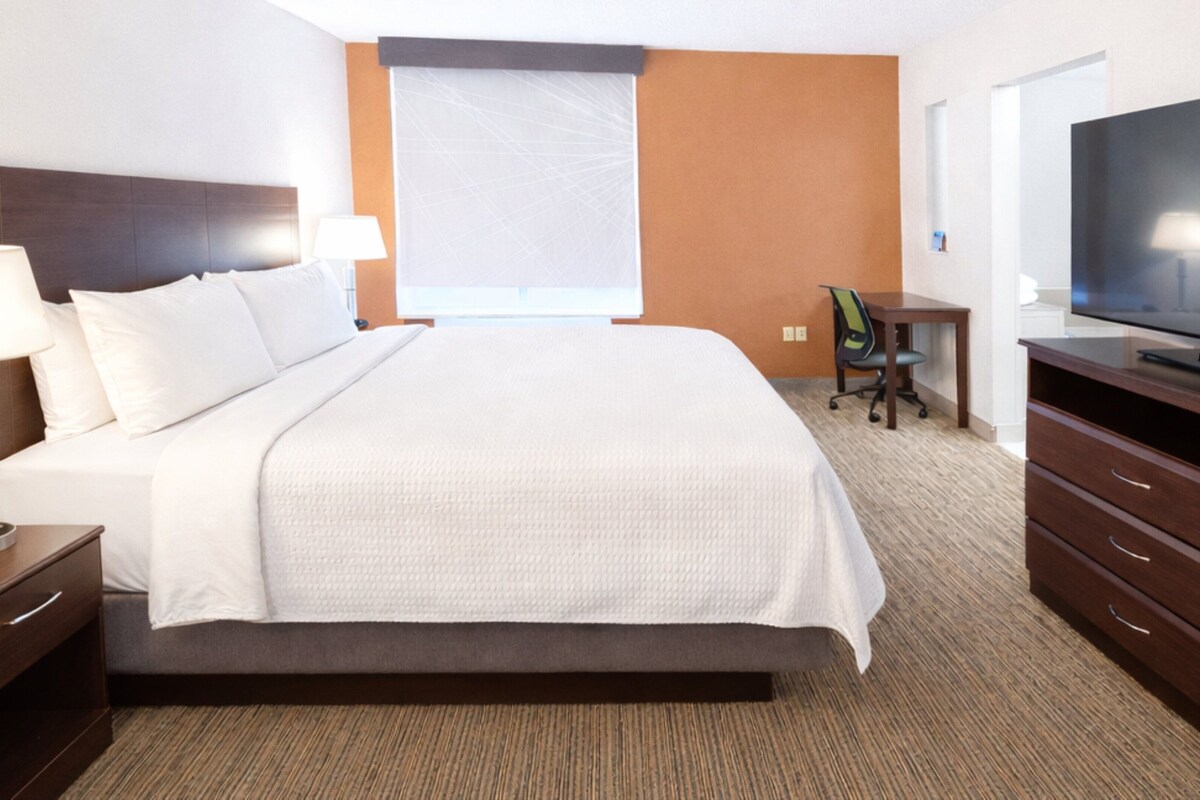 Una habitación de hotel con cama, escritorio, silla, televisor y ventana.