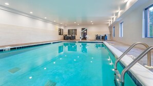 An indoor swimming pool with clear water, a tiled floor, and a metal ladder.