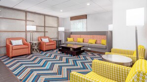 A modern living room with orange armchairs, a grey sofa with yellow cushions, a patterned rug, and a round coffee table.