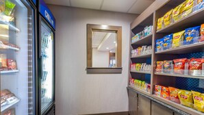 A snack bar with a refrigerated display and shelves stocked with various chips and snacks. - Hampton Inn Akron-South (Akron)