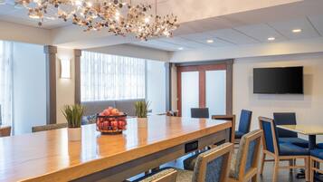 Una sala de conferencias moderna con una mesa de madera, sillas tapizadas en azul, una planta en maceta y un candelabro decorativo.