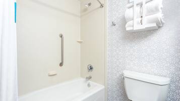 A bathroom with a bathtub, a toilet, and a shower with a handrail.