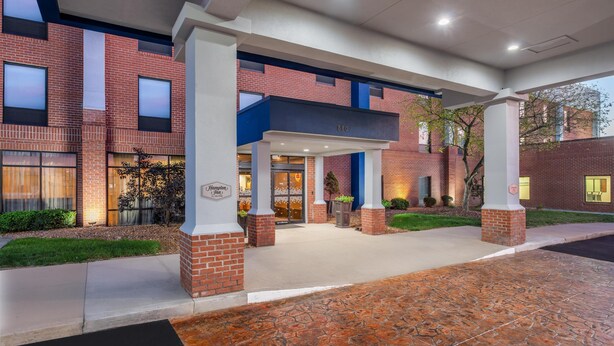 A hotel entrance with a brick facade, large windows, and a covered walkway. - Hampton Inn Akron-South (Akron)
