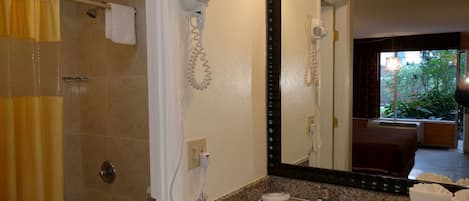 Un baño con ducha, lavabo, secador de pelo y espejo.