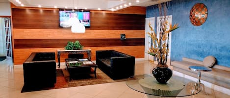 A hotel lobby with a reception desk, seating area, and a television screen.