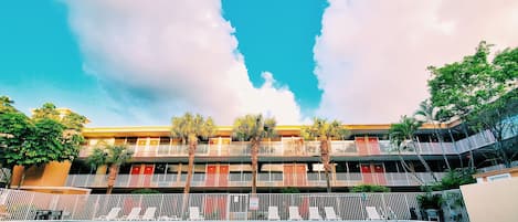 A hotel with multiple balconies, a swimming pool, and palm trees.
