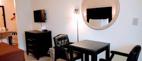 Une chambre d’hôtel comprenant un lit, un bureau, deux chaises, une télévision, un miroir et une commode.