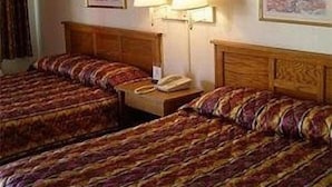 A hotel room with two beds, a bedside table with a lamp, and a painting on the wall. - Red Carpet Inn (Starke)