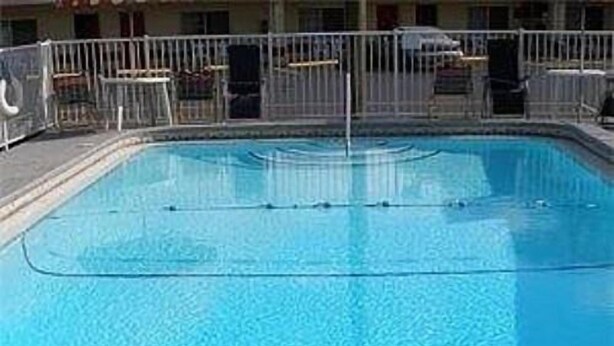 A clear blue swimming pool with a metal safety fence, surrounded by a building with multiple windows and balconies. - Red Carpet Inn (Starke)