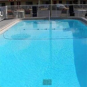 Una piscina azul clara con una valla metálica de seguridad, rodeada por un edificio con múltiples ventanas y balcones.