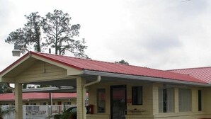 A single-story motel with a red roof and beige walls. It features a covered front porch and a small parking area. - Red Carpet Inn (Starke)