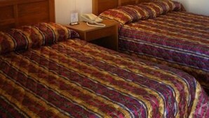 A hotel room with two beds, each with a patterned bedspread. There are two wall-mounted lamps on the nightstand between the beds. - Red Carpet Inn (Starke)