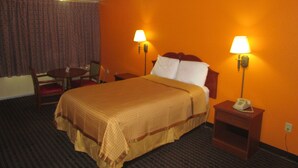 A hotel room with a large bed, two bedside lamps, a desk with a telephone, and a chair. - Red Carpet Inn (Augusta)