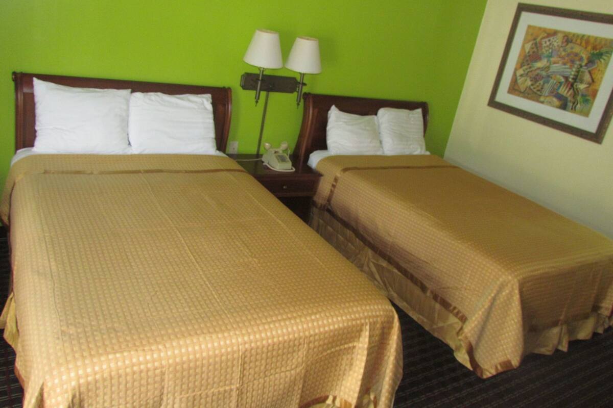 A hotel room with two beds, a green wall, and a painting.