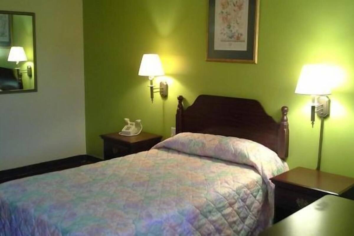 A hotel room with a bed, two bedside tables, a chair, and two wall-mounted lamps.