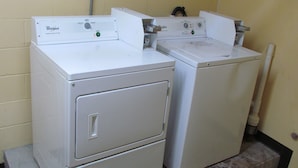 Two stacked Whirlpool dryers in a laundry room with a yellow wall and a concrete floor. - Red Carpet Inn (Augusta)