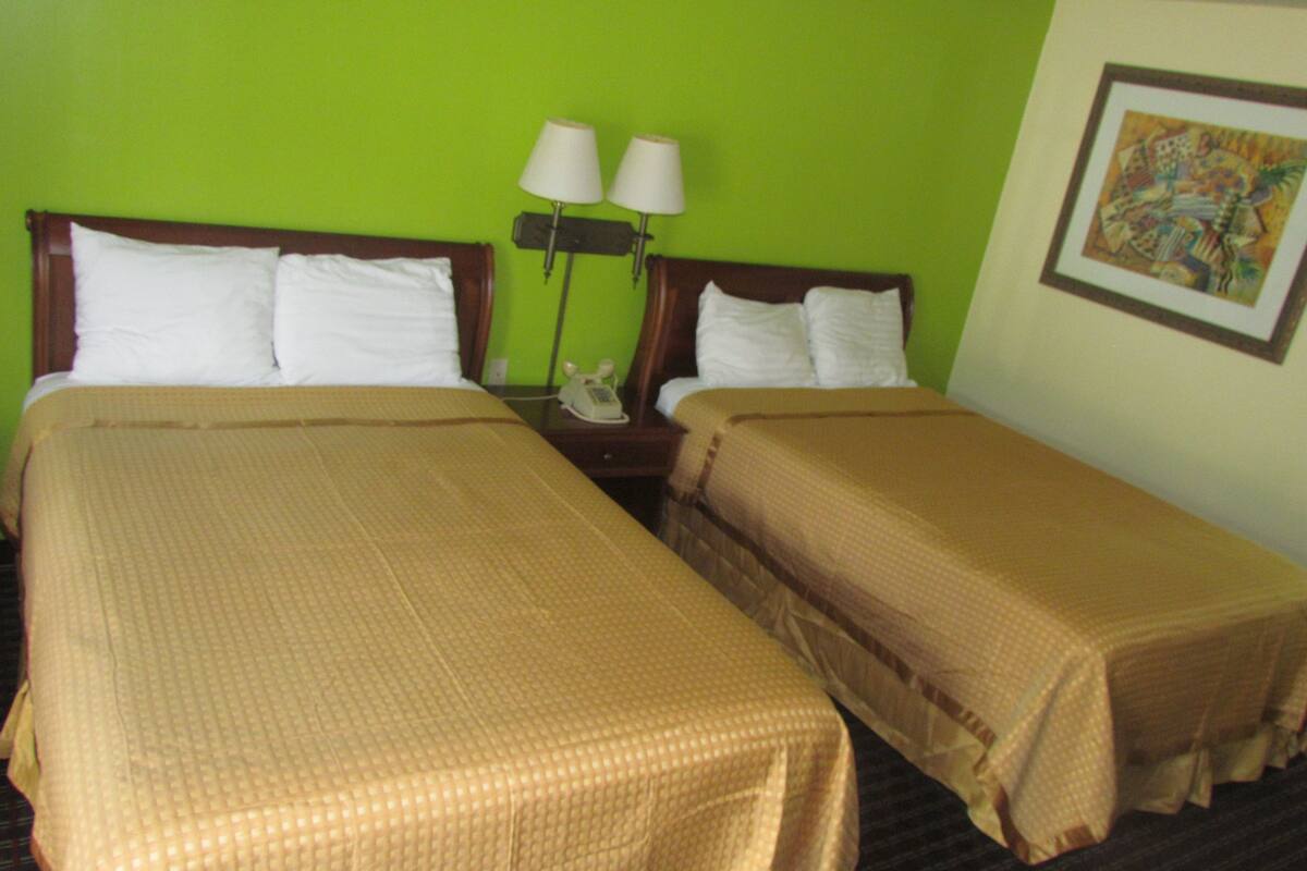 A hotel room with two single beds, a nightstand with a telephone, two wall-mounted lamps, and a painting on the wall.