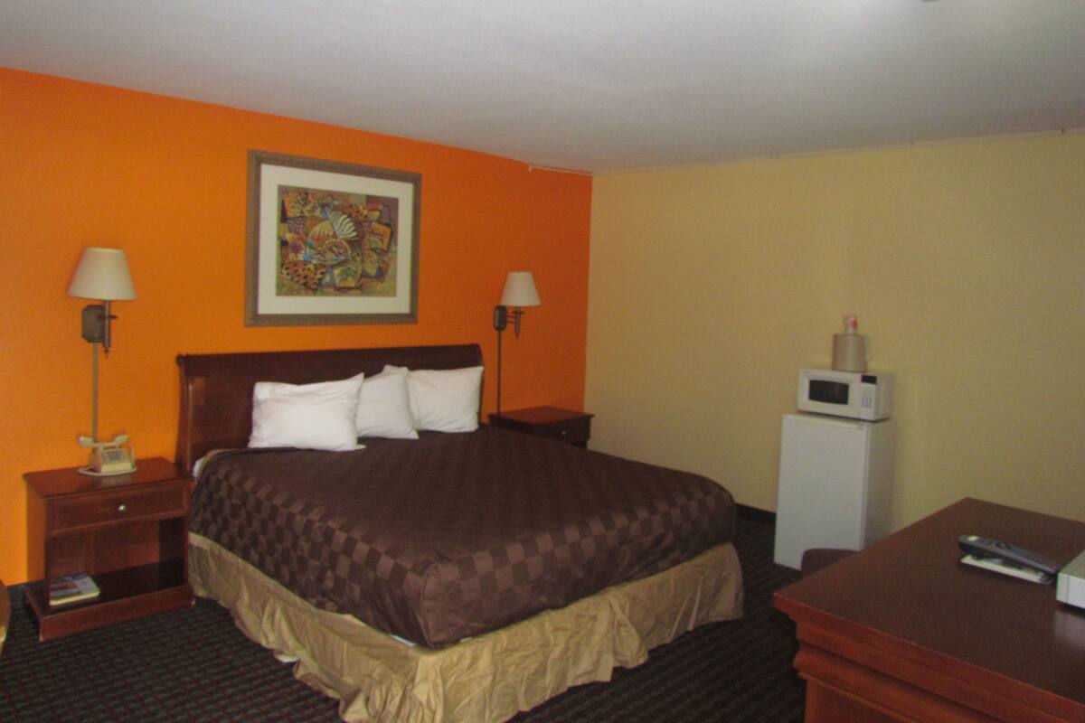 A hotel room with a bed, bedside lamps, a desk, a microwave, and a painting on the wall.