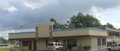 A building with a flat roof, a single-story structure, and a parking lot with two cars.