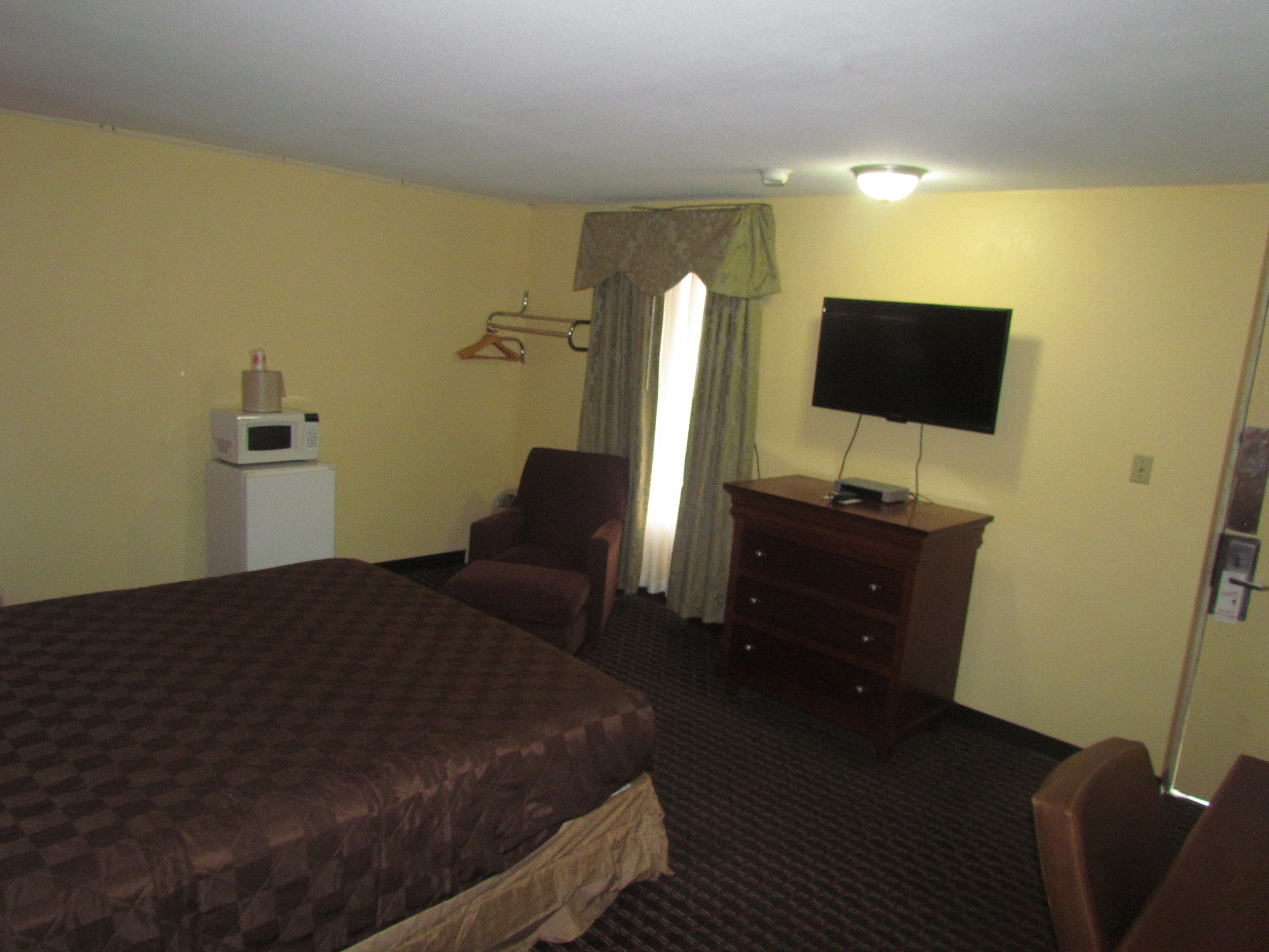 Une chambre d’hôtel avec un grand lit, une chaise, une commode, une télévision et un four à micro-ondes.