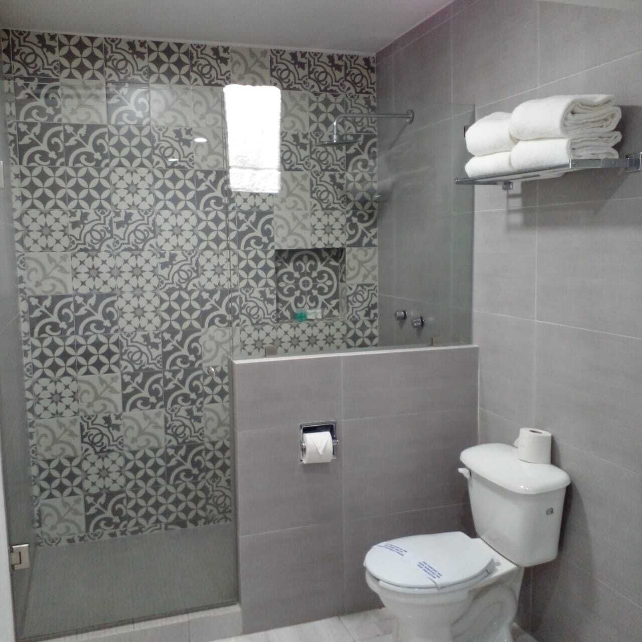 Ein Badezimmer mit gemusterten Fliesen, einer Toilette, einer Dusche und einem Handtuchhalter.