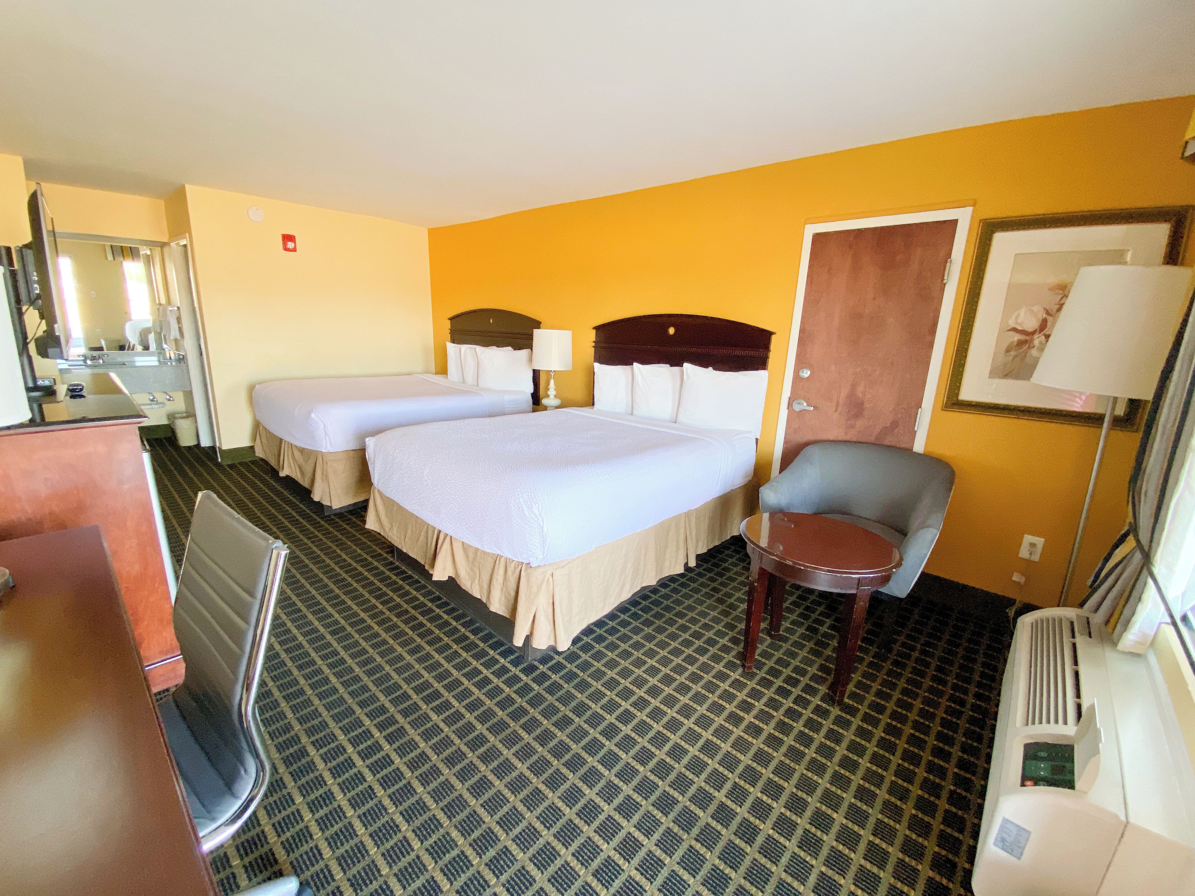 A hotel room with two beds, a desk, a chair, a mirror, and a door.