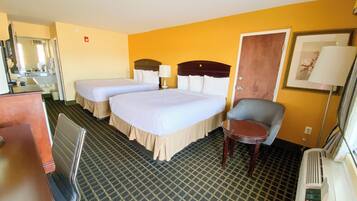 A hotel room with two beds, a desk, a chair, a mirror, and a door.