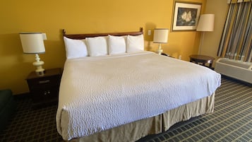 Quarto de hotel com cama grande, duas mesas de cabeceira, abajur, um quadro na parede e janela com cortinas.