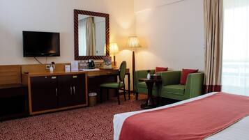 A hotel room with a bed, a desk with a chair, a television, a mirror, a lamp, and a window with curtains.