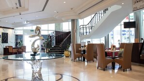A modern lobby with a glass table centerpiece, comfortable seating, a staircase, and large windows. - Dubai Grand Hotel by Fortune (Dubai)