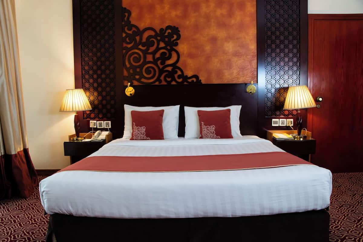 Une chambre d’hôtel avec un grand lit, deux tables de chevet avec des lampes, un téléphone et une moquette à motifs.