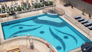 A swimming pool with a unique design, surrounded by lounge chairs and a sun umbrella. - Dubai Grand Hotel by Fortune (Dubai)
