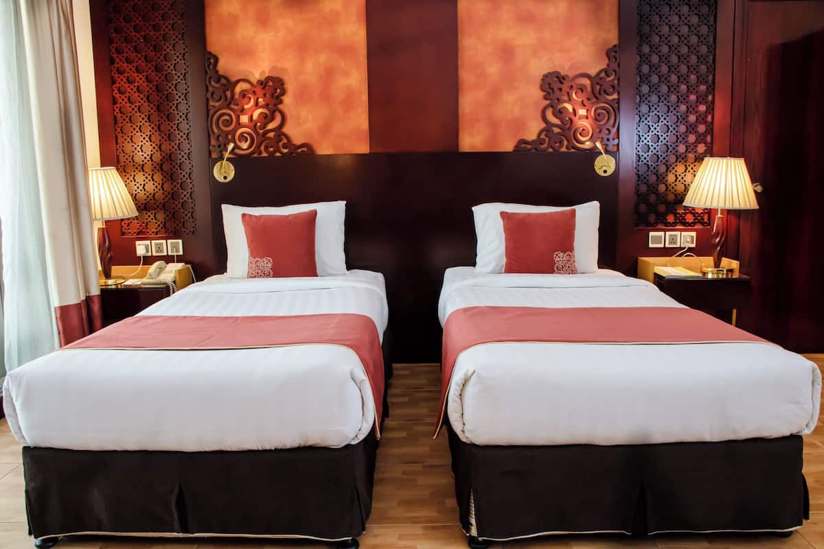 Une chambre d’hôtel avec deux lits, chacun agrémenté de draps blancs et de touches de couleur rouge, d’une tête de lit en bois et de panneaux décoratifs sur les murs.