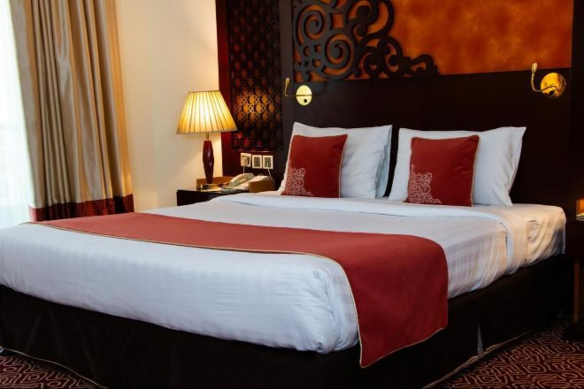 Een hotelkamer met een groot bed, een nachtkastje met een lamp en een decoratief hoofdbord.