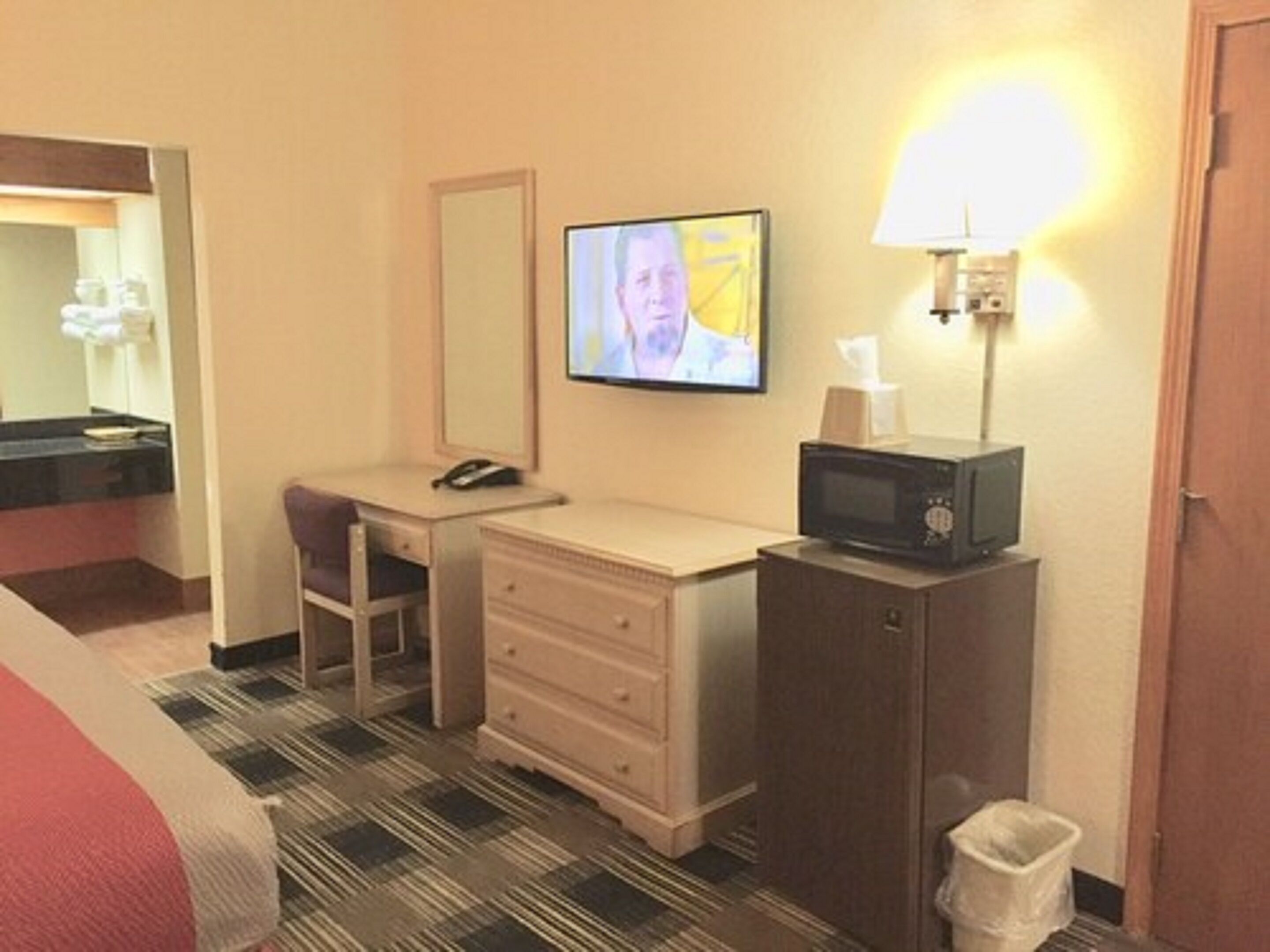 A hotel room with a bed, a desk with a telephone, a television, a microwave, and a trash bin.