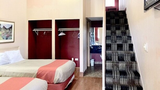 A bedroom with two beds, a wardrobe, a mirror, and a staircase. - Red Carpet Inn Great Lakes (North Chicago)