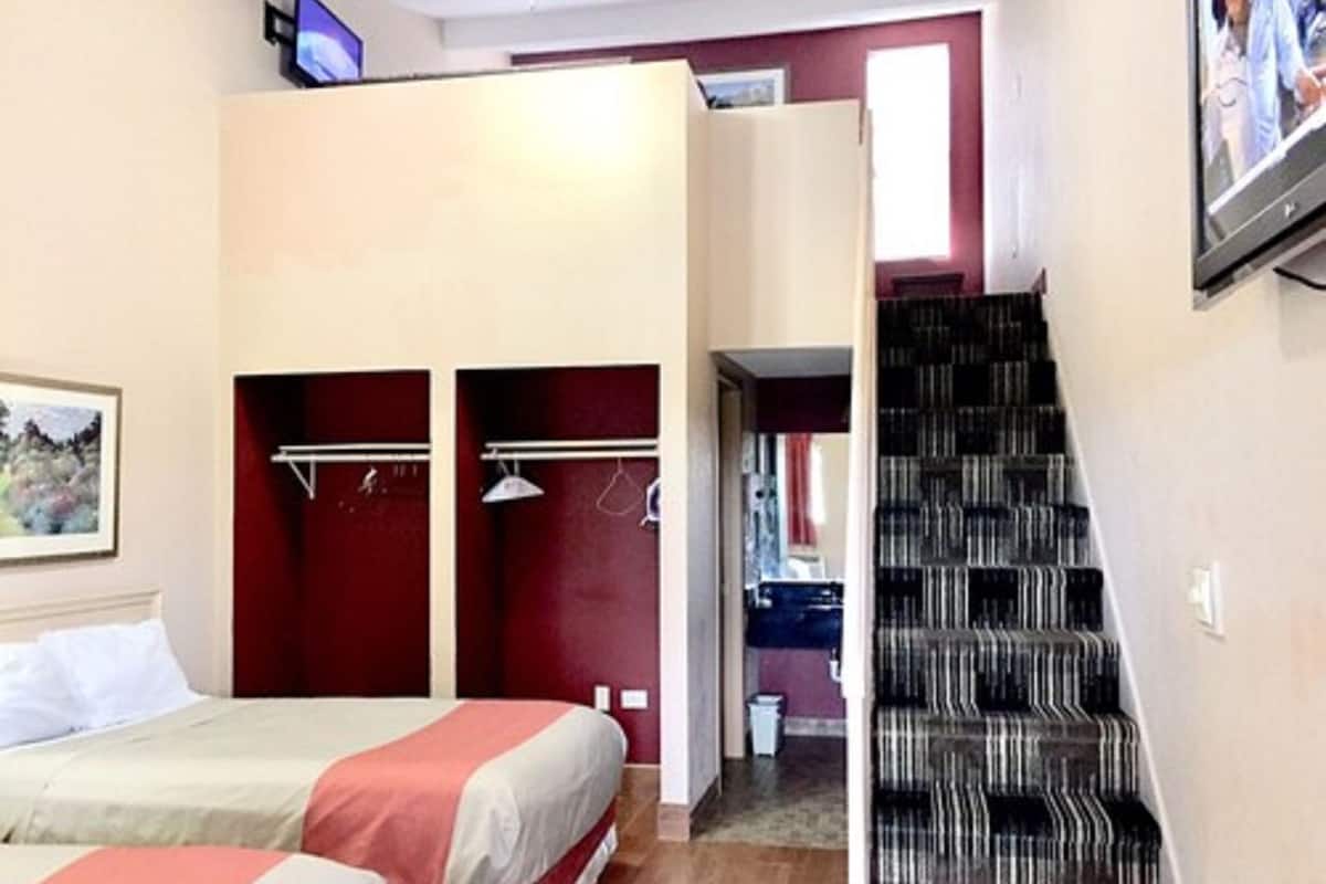 A bedroom with two beds, a wardrobe, a mirror, and a staircase.