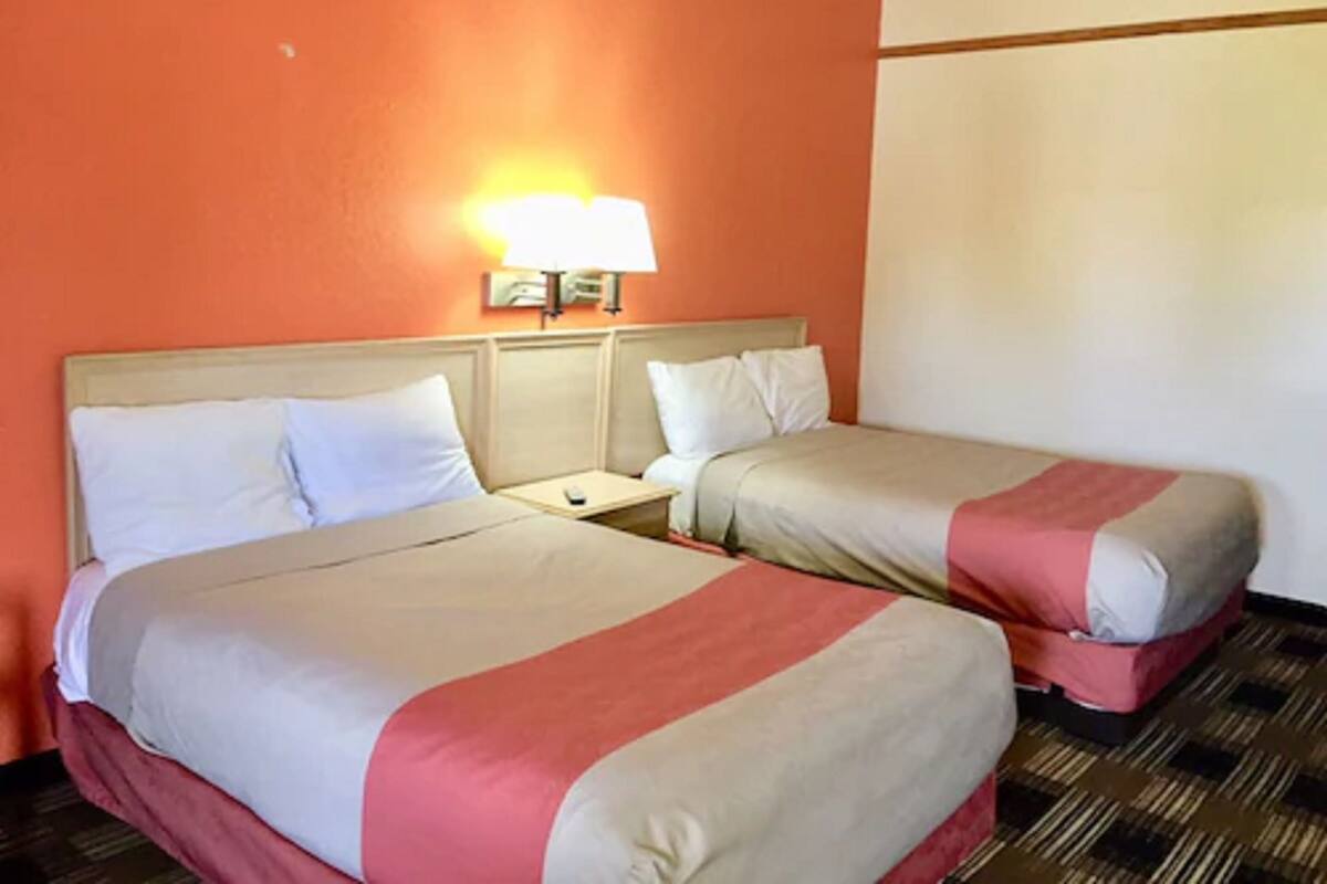 A hotel room with two beds, each with a headboard, a nightstand, and a wall-mounted lamp.