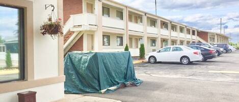 Un motel con zona de estacionamiento techada, una escalera cubierta y una fila de coches aparcados.