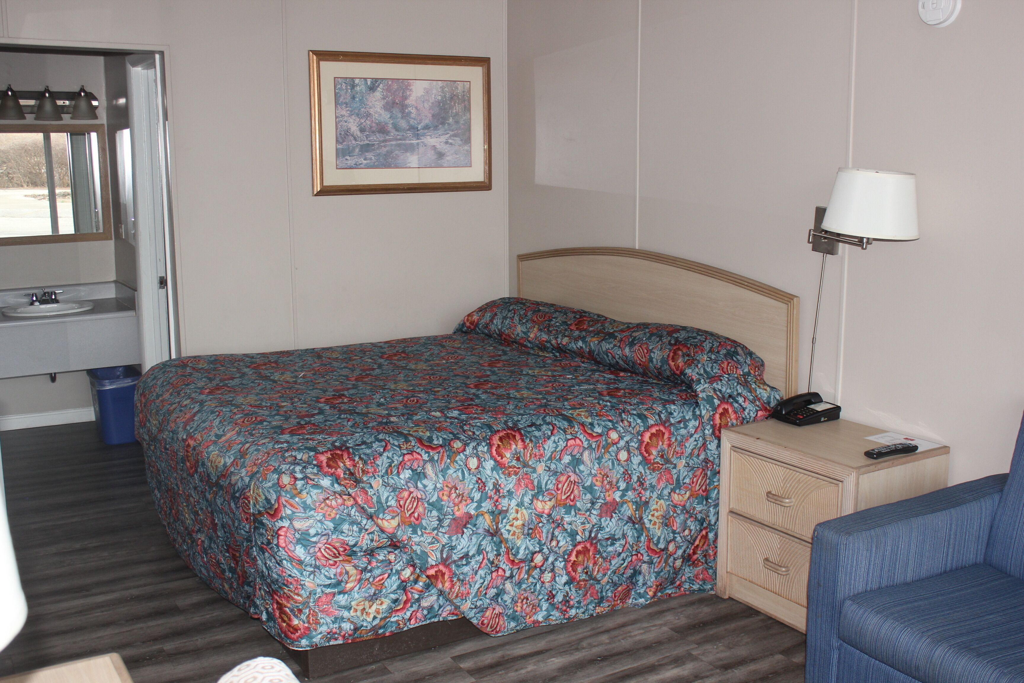 A bedroom with a bed, a bedside table with a lamp, a dresser, and a window with curtains.